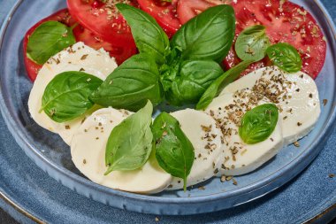 Dilimlenmiş taze domates, mozzarella ve fesleğen yapraklı klasik Caprese salatası. 