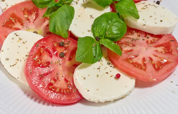 Dilimlenmiş taze domates, mozzarella ve fesleğen yapraklı klasik Caprese salatası.