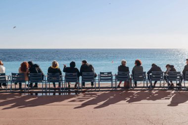 Nice, France - 15.01.2023 : People sitting on the famous blue chairs in Nice, in front of the sea on the Promenade des Anglais