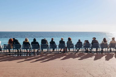 Nice, France - 15.01.2023 : People sitting on the famous blue chairs in Nice, in front of the sea on the Promenade des Anglais
