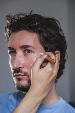 Handsome young man applying foundation to his face with a brus