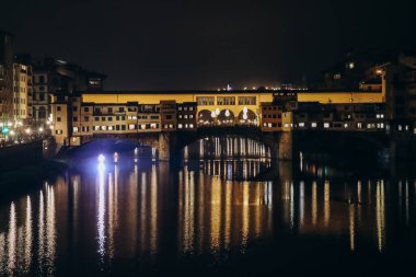Geceleyin Ponte Vecchio, Floransa, İtalya 'da Arno üzerindeki ortaçağ taşından kapalı-spandrel kemer köprüsü.