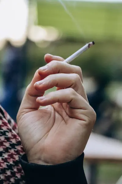 A man\'s hand holds a thin smoking cigarette
