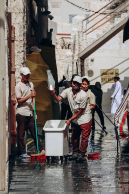 Doha, Katar - 1 Mayıs 2024: Katar 'ın Doha kentindeki Souq Waqif pazarında bir grup temizlikçi öğle yemeği sırasında sokakları yıkıyor.