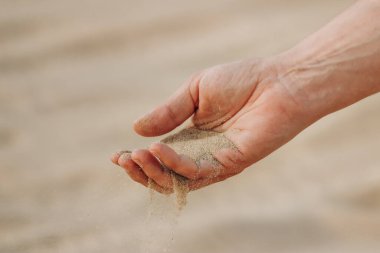 Bir adamın eli Katar 'daki çöle kum döküyor.