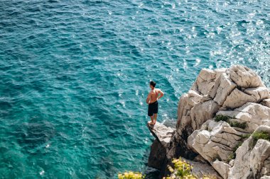 Genç bir adam Saint Jean Cap Ferrat yarımadasının kayalık kıyısında duruyor.