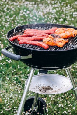 Chicken legs and merguez sausages cooking on a barbecue in the garden