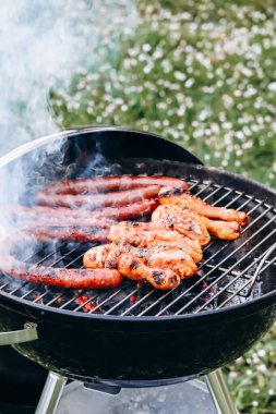 Chicken legs and merguez sausages cooking on a barbecue in the garden