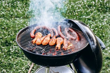Chicken legs and merguez sausages cooking on a barbecue in the garden