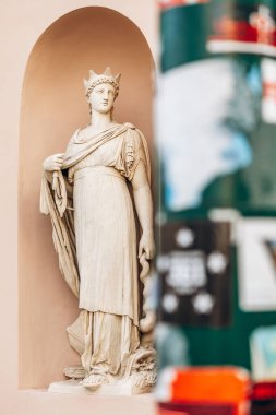 Trieste, İtalya - 18 Ağustos 2024: Ön planda kısmen bir sütun ve posterler tarafından çerçevelenmiş, taç ve asası olan klasik bir heykelin ayrıntılı bir görüntüsü.