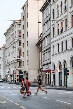Trieste, İtalya - 18 Ağustos 2024: Trieste şehir merkezinde karşıdan karşıya geçen üç kişi, arka planda kentsel trafik