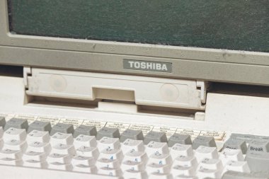 Trieste, İtalya - 18 Ağustos 2024: Tozlu bir klavyesi ve boş bir ekranı olan eski bir Toshiba dizüstü bilgisayarı, klasik bir ayarda sergilendi.