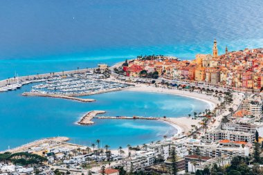 Menton 'un şehir merkezinin renkli tarihi binaları ve kasabayı çevreleyen mavi deniz manzarası.