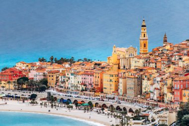 Menton 'un şehir merkezinin renkli tarihi binaları ve kasabayı çevreleyen mavi deniz manzarası.