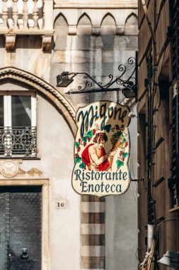 Cenova, İtalya - 22 Eylül 2024: Vintage Migone Ristorante Enoteca tabelası Piazza San Matteo 'daki çizgili ortaçağ kemerleri ve taş basamaklarının yanında asılı.