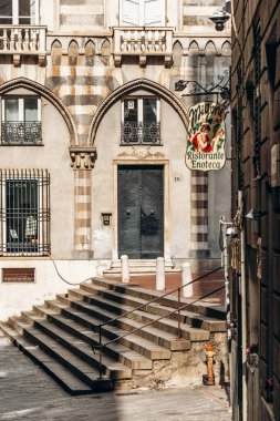 Cenova, İtalya - 22 Eylül 2024: Vintage Migone Ristorante Enoteca tabelası Piazza San Matteo 'daki çizgili ortaçağ kemerleri ve taş basamaklarının yanında asılı.