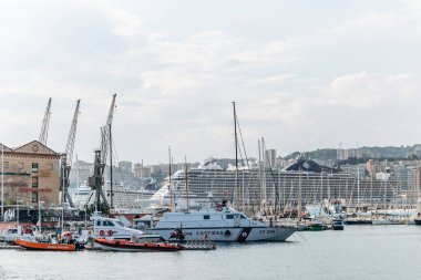 Cenova, İtalya - 22 Eylül 2024 Sahil Güvenlik tekneleri, yelkenliler ve büyük bir yolcu gemisi şehrin ufuk çizgisi ile dolu limana yanaştı..