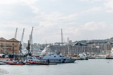 Cenova, İtalya - 22 Eylül 2024 Sahil Güvenlik tekneleri, yelkenliler ve büyük bir yolcu gemisi şehrin ufuk çizgisi ile dolu limana yanaştı..