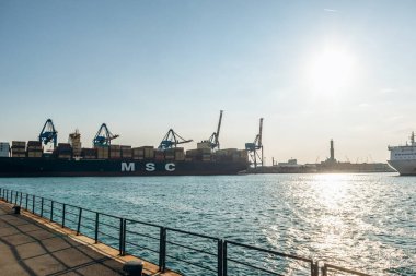 Ceneviz, İtalya - 22 Eylül 2024: Endüstriyel limana vinçlerle kenetlenmiş büyük konteyner gemisi ve açık gökyüzü altında yüklenmiş kargo.