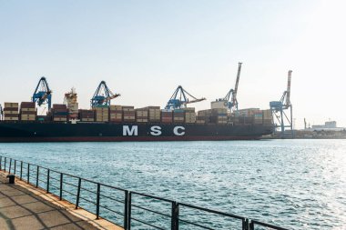 Ceneviz, İtalya - 22 Eylül 2024: Endüstriyel limana vinçlerle kenetlenmiş büyük konteyner gemisi ve açık gökyüzü altında yüklenmiş kargo.