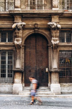 Cenova şehir merkezindeki tarihi taş binanın önünden geçen insanların bulanık figürleri