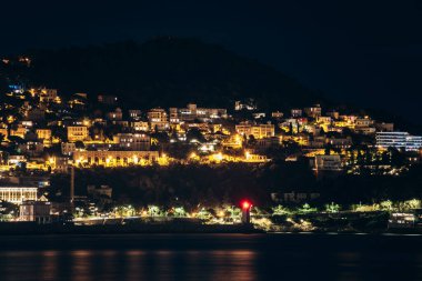 Nice 'in Fransız Rivierası' ndaki gece manzarası, yamaçtaki evler ve limandaki kırmızı ışıklı deniz feneri..