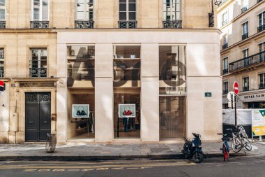 Paris, Fransa - 23 Şubat 2025: Saint-Honore sokağındaki Acne Stüdyoları butik ön cephe, büyük cam pencereli minimalist taş dış cephe, vitrinde el çantaları, park edilmiş scooter ve bisikletler