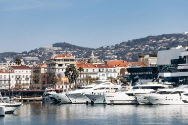 Cannes, Fransa - 8 Mart 2025: Arka planda Palais des Festivals ve şehir tepeleriyle Eski Liman 'da balıkçı tekneleri ve yatlar.
