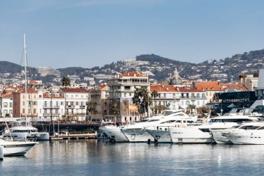 Cannes, Fransa - 8 Mart 2025: Arka planda Palais des Festivals ve şehir tepeleriyle Eski Liman 'da balıkçı tekneleri ve yatlar.