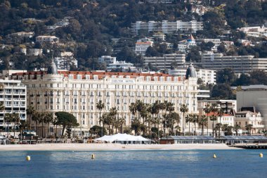 Cannes, Fransa - 8 Mart 2025: Croisette rıhtımında Iconic Carlton Oteli Palmiye ağaçları ve şehir tepeleri arka planda.