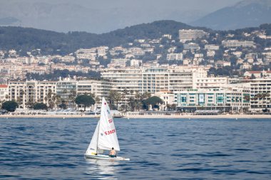 Cannes, Fransa - 8 Mart 2025: Sakin denizde yelkenli ve arka planda tepeler.