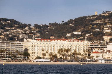 Cannes, Fransa - 8 Mart 2025: Croisette rıhtımında Iconic Carlton Oteli Palmiye ağaçları ve şehir tepeleri arka planda.