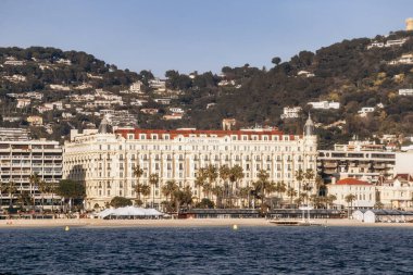 Cannes, Fransa - 8 Mart 2025: Croisette rıhtımında Iconic Carlton Oteli Palmiye ağaçları ve şehir tepeleri arka planda.