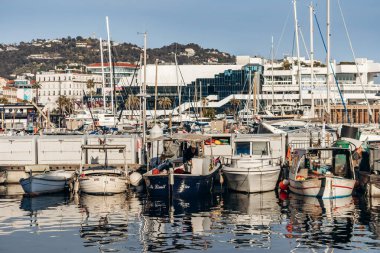 Cannes, Fransa - 8 Mart 2025: Arka planda Palais des Festivals ve şehir tepeleriyle Eski Liman 'da balıkçı tekneleri ve yatlar.