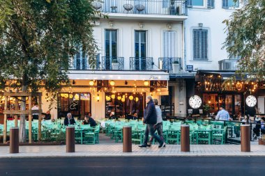 Cannes, Fransa - 8 Mart 2025: Turkuaz sandalyeli açık kafe terası ve şehir merkezinde parlayan ışıklar.