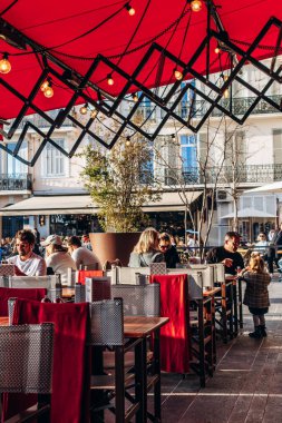 Cannes, Fransa - 8 Mart 2025: Şehir merkezinde kırmızı bir tente altında dinlenen insanlarla birlikte açık kafe terası.