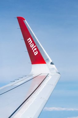Valletta, Malta - 9 Nisan 2025: Kırmızı kanatlı Air Malta uçağı kanadı ve bulutların üzerinden uçarken yolcu penceresinden logosu görüldü.