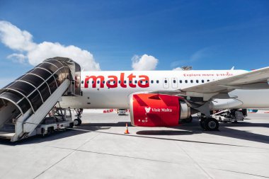 Luqa, Malta - 9 Nisan 2025: Air Malta uçağı Malta Uluslararası Havaalanı 'nda mavi gökyüzü altında yolcu biniş rampasına park edilmiş..