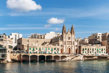 Balluta Körfezi, Malta - 9 Nisan 2025: Neo-gotik Karmelit Kilisesi, geleneksel ve modern binalarla çevrili olan St Julian 's ve Sliema arasındaki Balluta Körfezi' nin rıhtımında yer almaktadır.