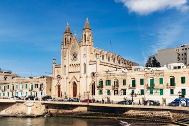 Balluta Körfezi, Malta - 9 Nisan 2025: Neo-gotik Karmelit Kilisesi, geleneksel ve modern binalarla çevrili olan St Julian 's ve Sliema arasındaki Balluta Körfezi' nin rıhtımında yer almaktadır.