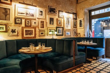 Valletta, Malta - 9 Nisan 2025: Taproom Valletta restoranının rahat iç mekanı konforlu deniz mavisi kadife kabinleri, yemek için hazırlanan yuvarlak masalar, klasik lambalar ve eklektik çerçevelerden oluşan bir galeri duvarı