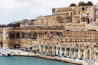 Valletta, Malta - 10 Nisan 2025: Grand Harbour 'da demirli feribot ve yolcu gemileriyle tarihi Valletta rıhtım ve tahkimat manzarası