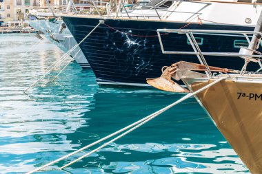 Birgu 'daki marinanın turkuaz suyuna yansıyan lüks yat yayı ve çapaların yakın görüntüsü.