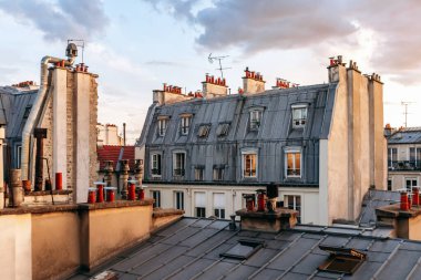 Classic Paris rooftops with chimneys and mansard windows at sunset.
