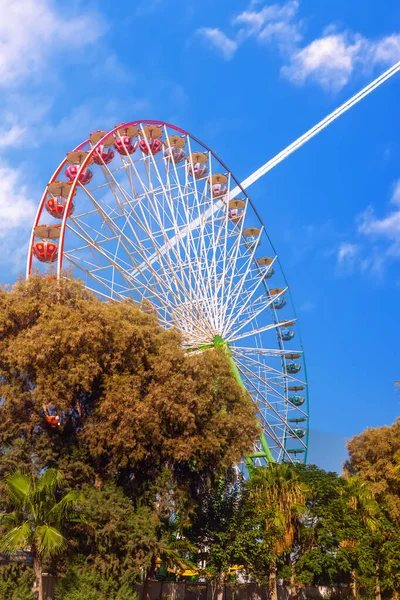 Ferris wheel on the background of an airplane flying through the blue sky. Ayia Napa. Cyprus.