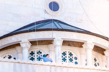 Podgorica, Karadağ - 08 Ağustos 2023: Mavi gömlekli bir çan çalıcısı kilisede çanları çalıyor.