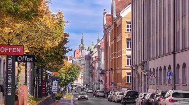 St. Gallen, İsviçre - 14 Ekim 2024: Klasik mimarisi, renkli yeşilliği, park edilmiş arabaları ve açık mavi gökyüzünün altındaki kilise kuleleri olan tarihi bir İsviçre şehrinde sonbahar caddesi