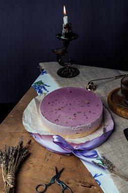 Kısa hamurlu lavantalı kek, kırsal tarzda mor jöle, cam bardakta çay, ahşap arka planda lavanta tatlısı, yassı pasta, mum, konforlu çay partisi.