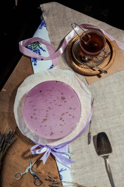 Kısa hamurlu lavantalı kek, kırsal tarzda mor jöle, cam bardakta çay, ahşap arka planda lavanta tatlısı, yassı pasta, mum, konforlu çay partisi.