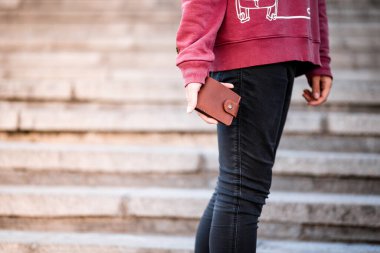 Pembe kapüşonlu ve kot pantolonlu genç bir kadın sokakta yürüyor.